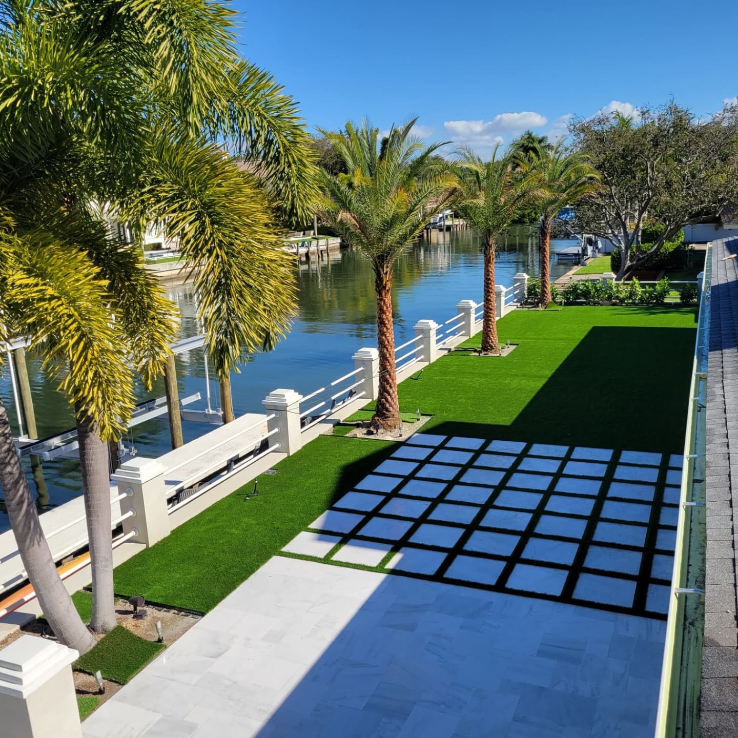 Turf terrace with a grid of square pavers along a palm-lined canal