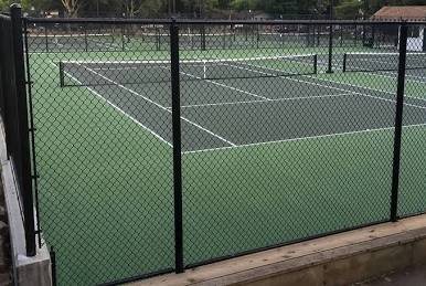 Black chain link fence enclosing a green tennis court