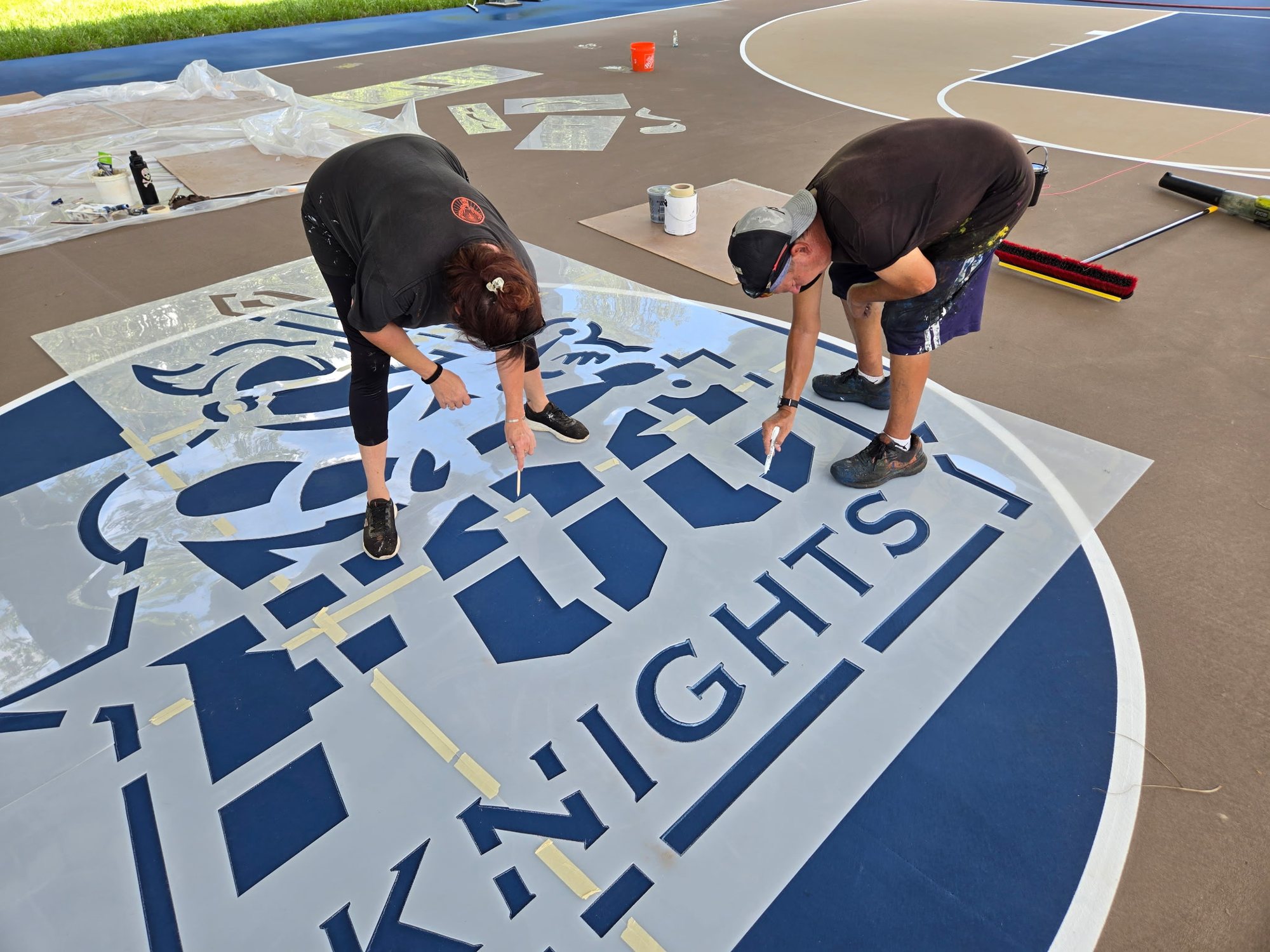 Two Golf Coast Sports crew members hand-painting a Knights logo at center court