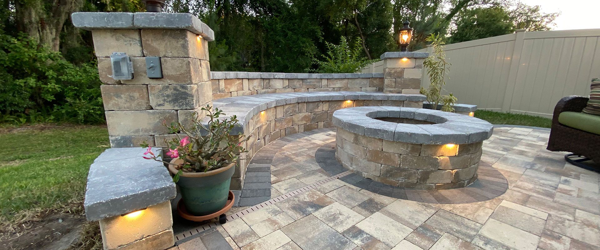 Paver patio with lit stone columns, a curved seating wall and a round fire pit
