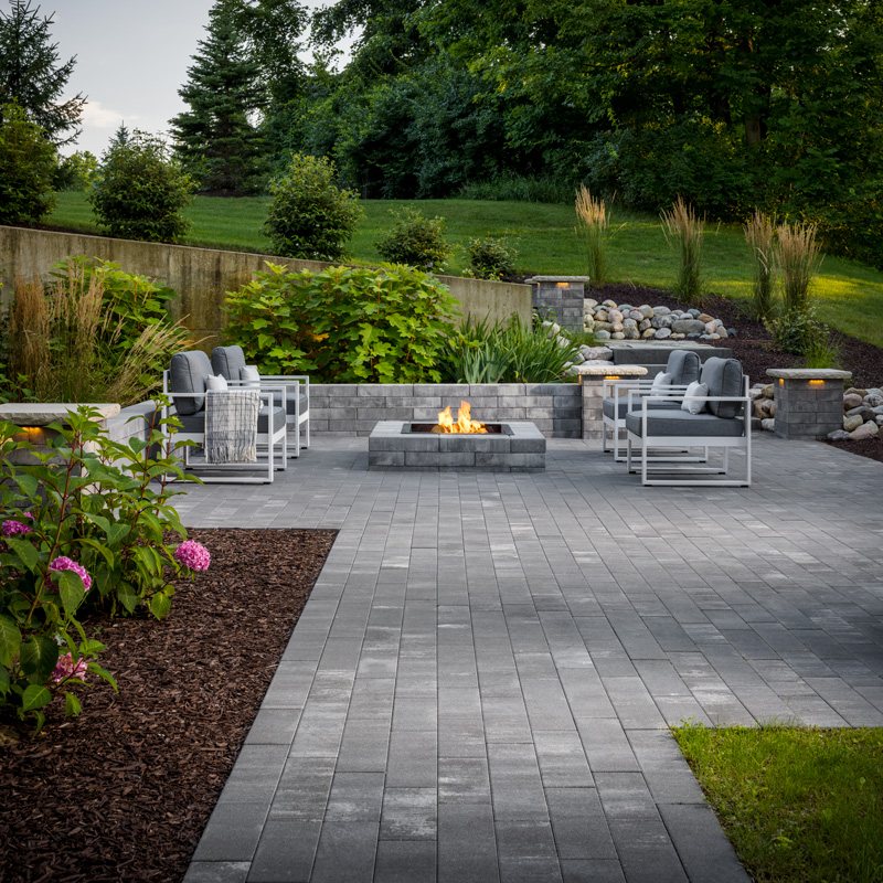 Large paver patio with modern furniture and a linear fire table