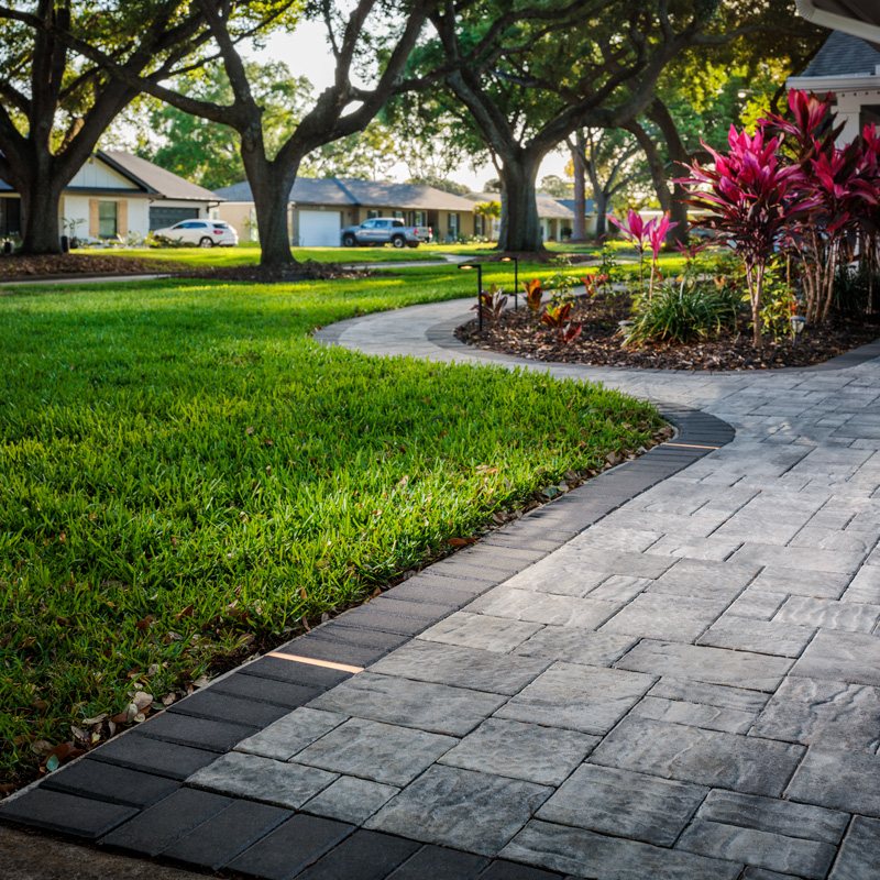 Curved dark paver walkway through a lawn under oak trees