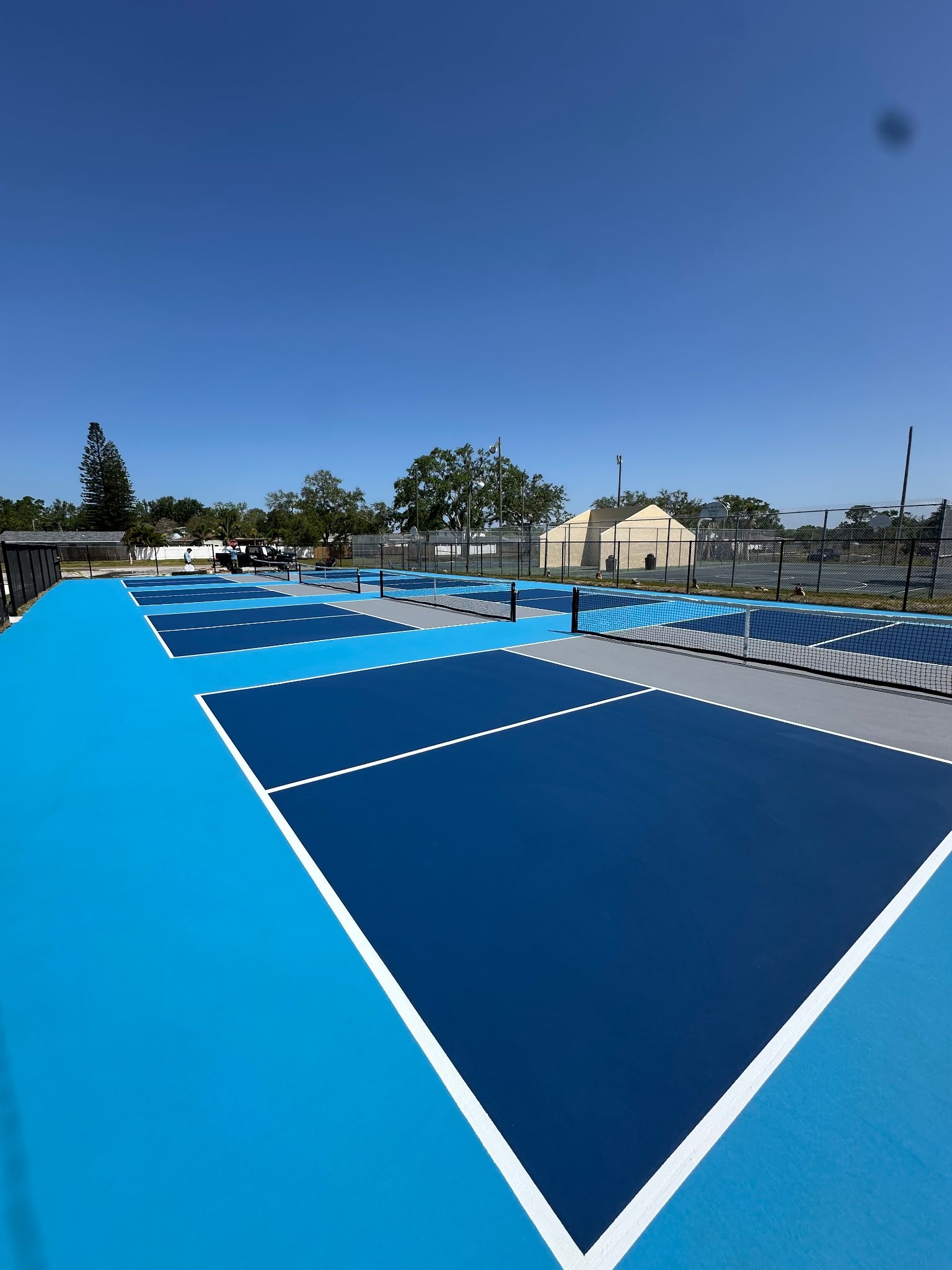 Row of blue pickleball courts under clear sky