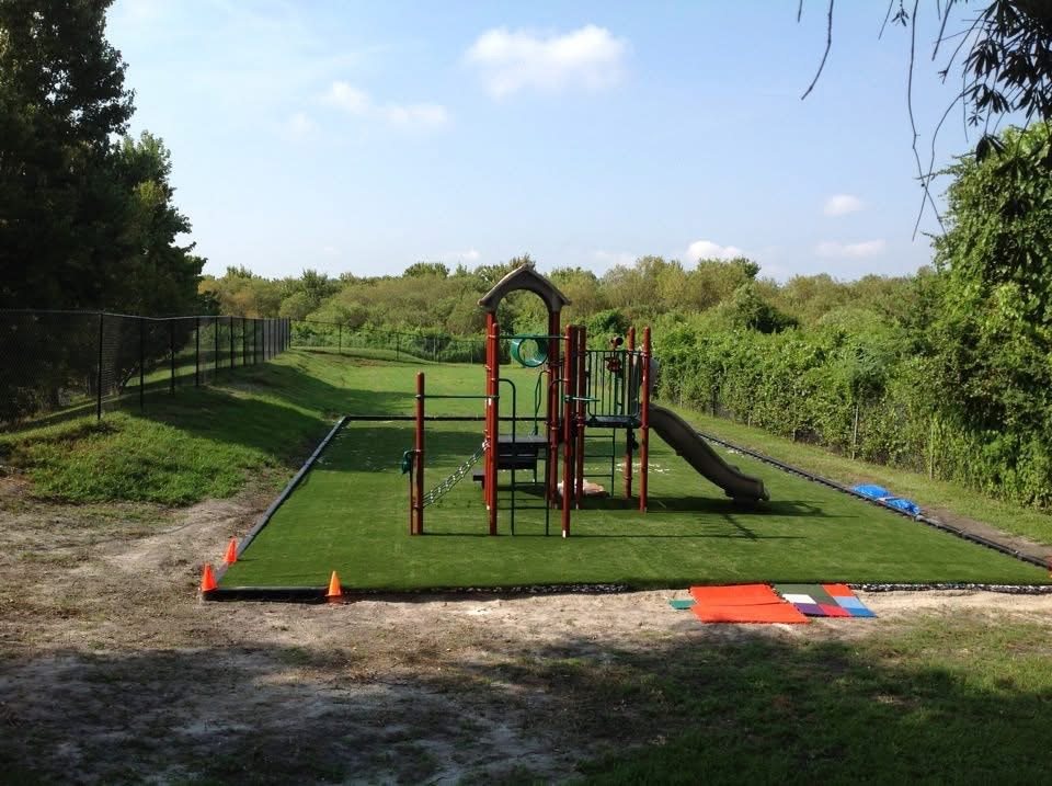 Playground on a turf pad beside a wooded park