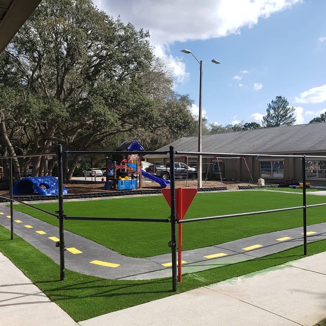 School play yard with turf, a painted trike track and playground under oak trees