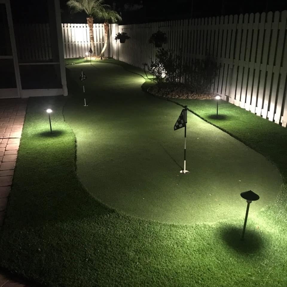 Narrow side-yard putting green lit at night by path lights