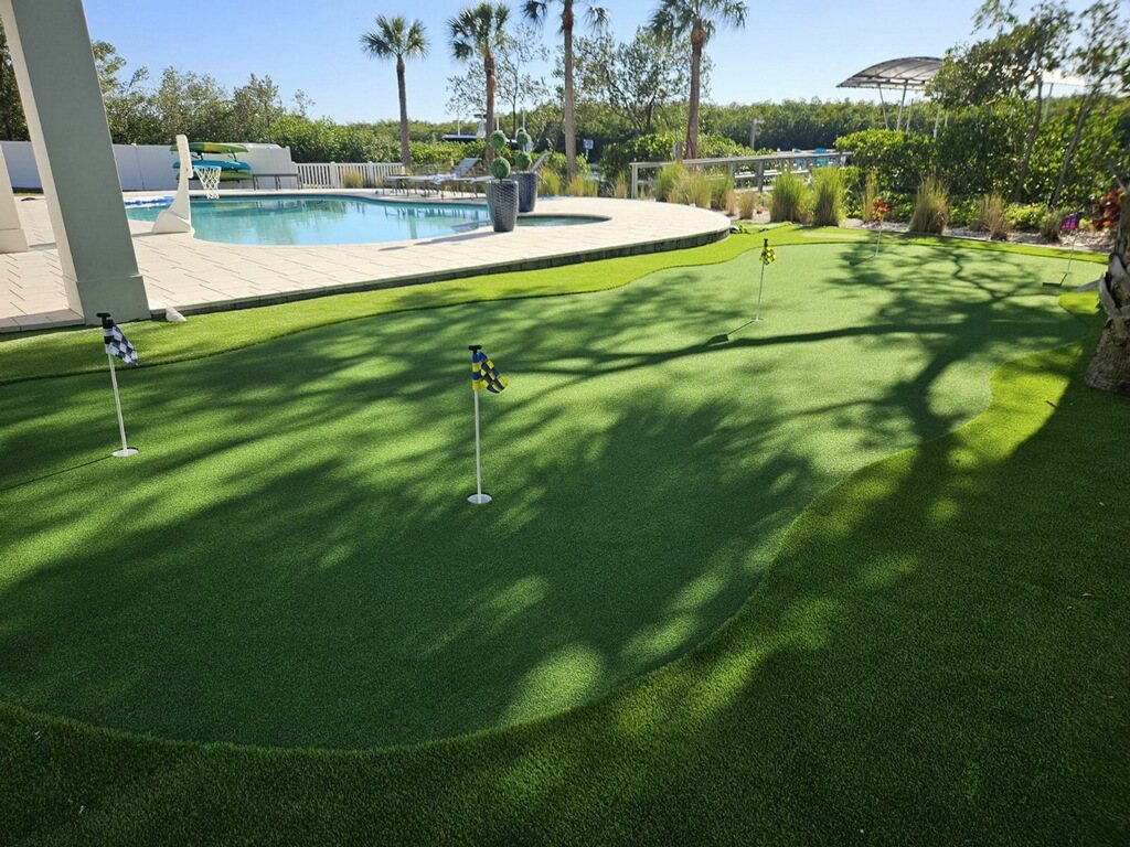 Putting green beside a pool deck with palm shadows and waterfront views