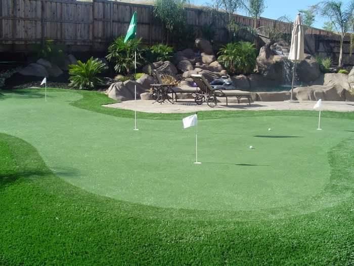Backyard putting green with several flags below a rock waterfall and pool lounge