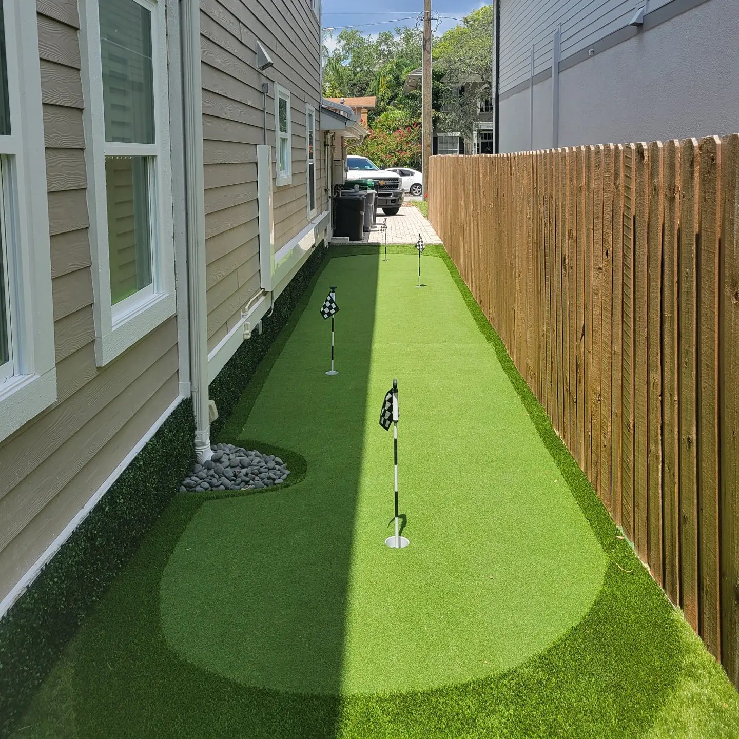 Narrow putting green along a wood fence beside a home