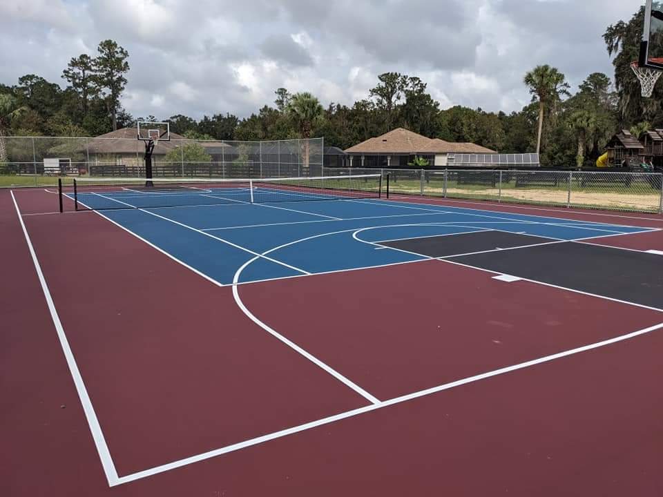Red and blue tennis courts at a club with trees behind