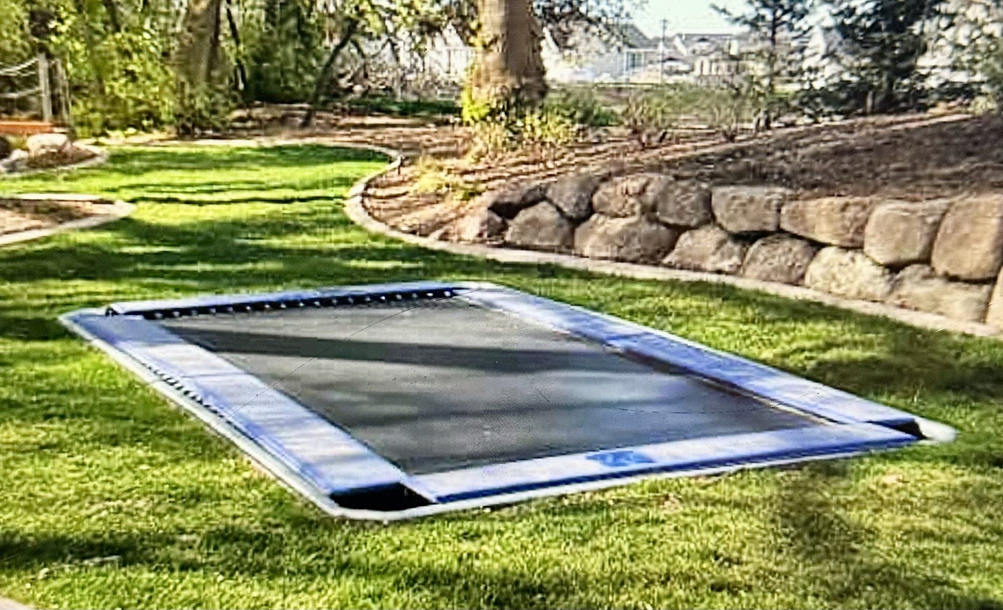 In-ground trampoline set level in turf beside a stacked stone wall