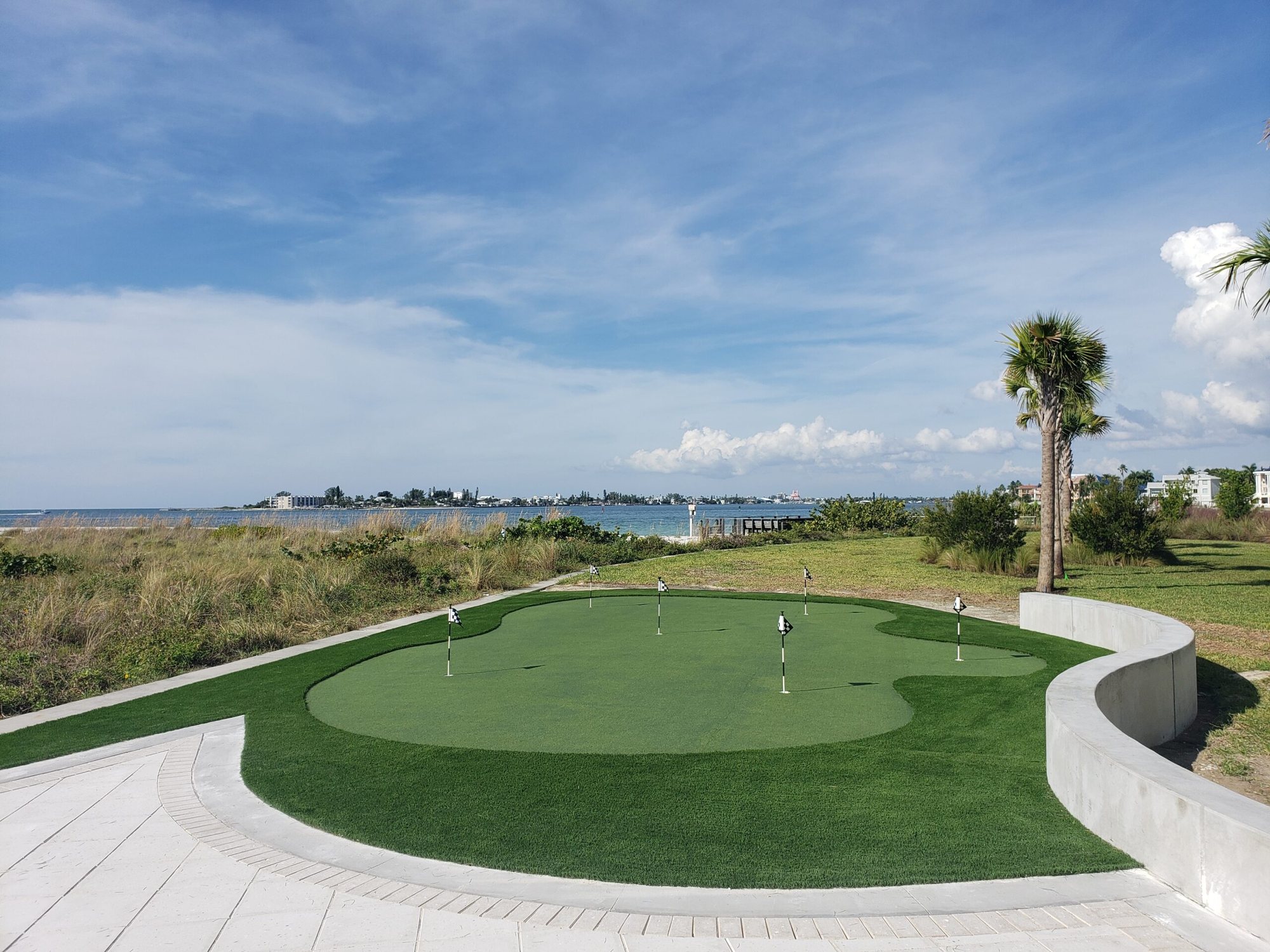 Contoured putting green on a waterfront lot with a curved white seawall and open bay beyond