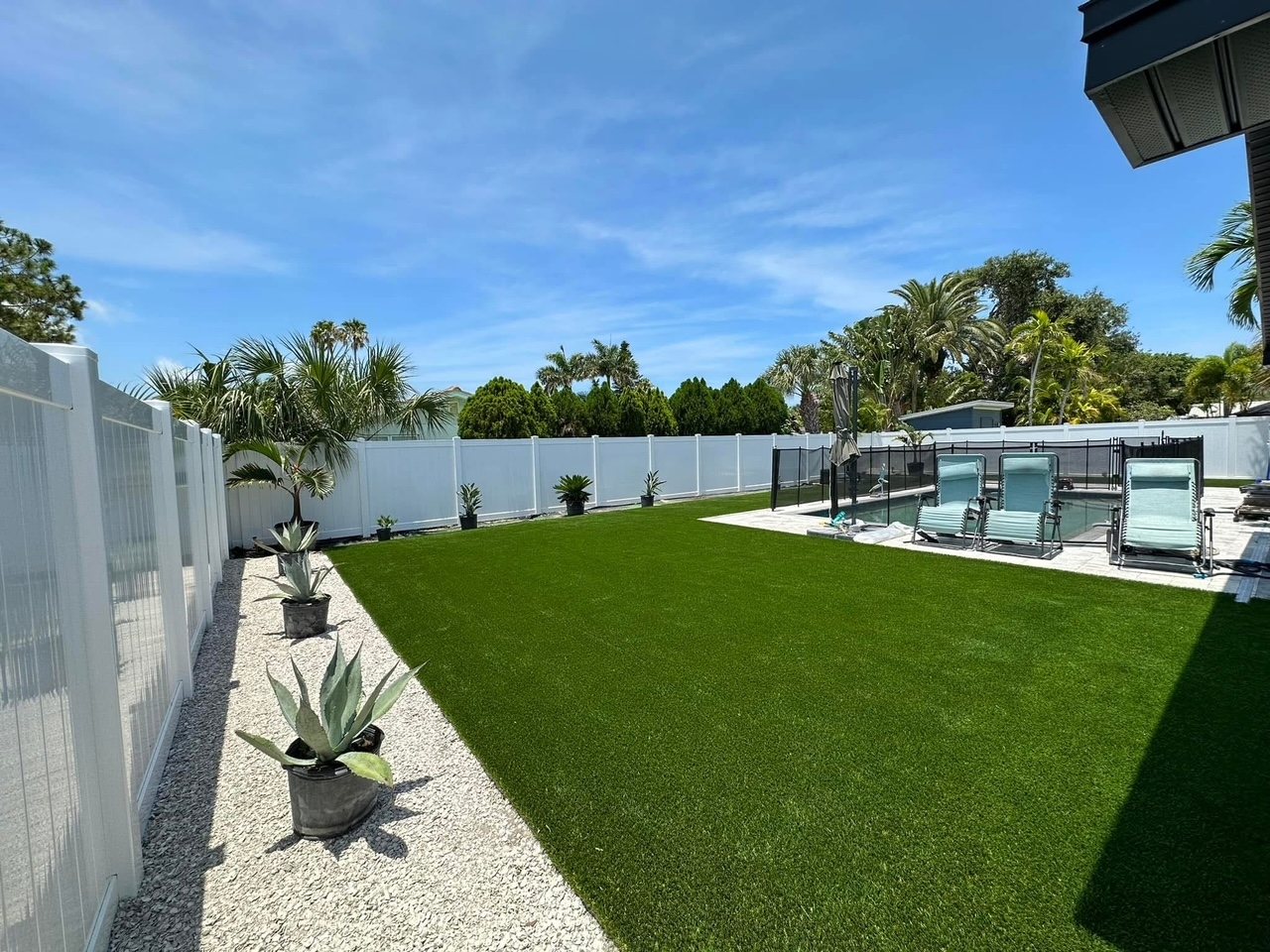 Wide turf yard along a white fence leading to a pool deck